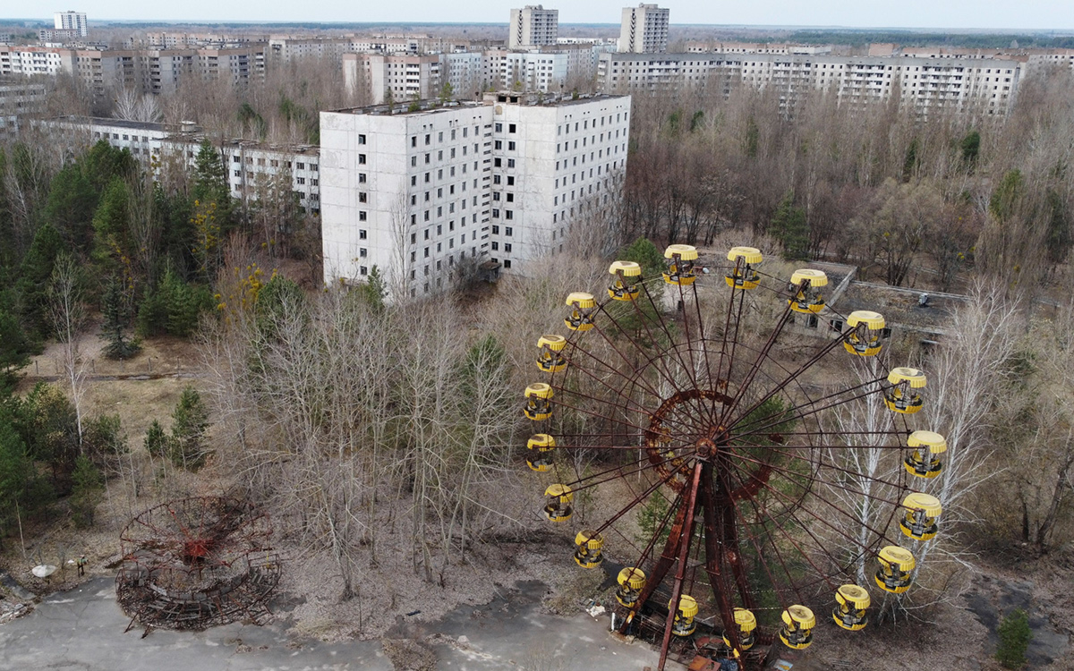 35 лет назад произошла огромная трагедия, изменившая жизнь не только сотен тысяч украинцев, но и жителей планеты в целом. Взрыв на 4-ом энергоблоке в апреле 1986 года загрязнил атмосферу радиацией, и последствия человеческой халатности планета ощущает на себе до сих пор. Чернобыль находится всего в 2-х километрах от городка Припять, который на то время подавал огромные надежды и с радостью принимал новых жителей. К сожалению, ему не судьба была стать городом, в котором кипит жизнь: после взрыва более 100 тыс. жителей были эвакуированы, а 30-километровая зона стала зоной отчуждения. Работу ЧАЭС остановили в 2000 году, но полноценная остановка работы энергоблоков может занять еще очень много времени. Саркофаг, построенный над 4-м энергоблоком, полностью достроили в 2019 году и ввели в эксплуатацию. Работы по реконструкции саркофага и остановке работы ЧАЭС продолжаются до сих пор, а туроператоры организовывают экскурсии в зону отчуждения. Много туристов хочет попасть в Чернобыль и посмотреть на все своими глазами. Спустя больше чем 30 лет природа победила цивилизацию и поглотила город. Попав туда, кажется, что здесь всегда был непролазный лес и только заброшенные дома каким-то непонятным образом здесь оказались. Там, где раньше были кафе, кинотеатр, парки с развлечениями - сейчас растут деревья. Дома выглядят устрашающе, а квартиры внутри уже не напоминают уютные помещения, в которых раньше жилы люди. Время, осадки и погода повлияли на состояние квартир - уже нет следа от какого-либо ремонта, все некрасивое и заброшенное. Очень сильно такому внешнему виду домов и квартир в частности помогли мародеры: они вывезли отсюда все ценное (металл, вещи, ценности и все то, чем можно поживиться и на чем заработать денег) и оставили после себя разруху и бардак. Зайдя в любую из квартир, сразу понимаешь, что здесь побывал человек с желанием наживы: все разбросанное, исковерканное, батареи отсутствуют, как и большинство металлических предметов в квартирах. Все лежит вверх дном. Люди, которых насильно эвакуировали из их домов, верили, что когда-то вернутся сюда, но их мечте не суждено было сбыться. Большинство их вещей осталось в квартирах как приманка для людей, желающих поживиться за чужой счет. Когда оказываешься в Припяти, кажется, что только вчера здесь бурлила и кипела жизнь: молодежь гуляла по парку, школьники шли учиться, старики сидели на лавочках и говорили о своем, а сегодня ничего этого здесь нет. Только шум листьев и тоскливое молчание города, который когда-то должен был стать пристанью для спокойной, размеренной и счастливой жизни. Туристы, чтобы попасть в зону отчуждения, проходят строгий досмотр и не могут быть на территории Припяти и Чернобыля в открытой одежде. Также они не могут попасть туда самовольно - пребывание разрешено только в присутствии гида. Находиться здесь можно не более чем 5 дней, но поток туристов просто огромен: после выхода в 2019-м году сериала "Чернобыль" количество желающих попасть сюда и увидеть все своими глазами выросло в несколько раз. Больше 125 тыс. человек посетило зону отчуждения и количество туристов не уменьшается.